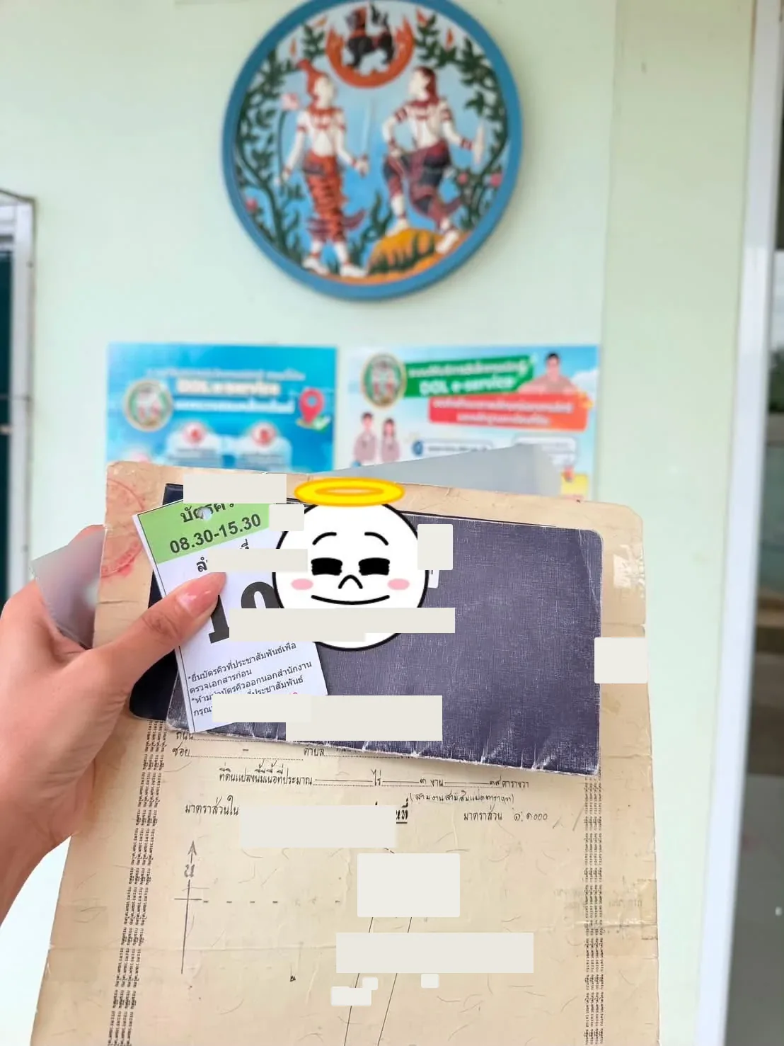 มือถือบัตรคิวและเอกสารหน้าสำนักงานที่ดิน มีป้ายบริการ DOL e-Service ด้านหลัง