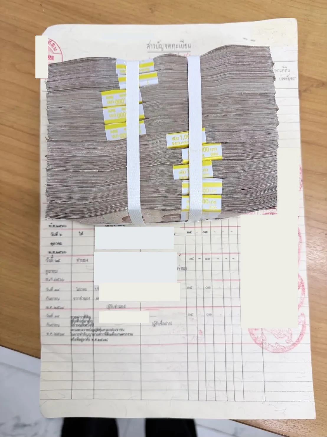 ธนบัตรรัดแถบวางบนสารบัญจดทะเบียนในวันทำธุรกรรม ปิดทับชื่อและข้อมูลเจ้าพนักงาน